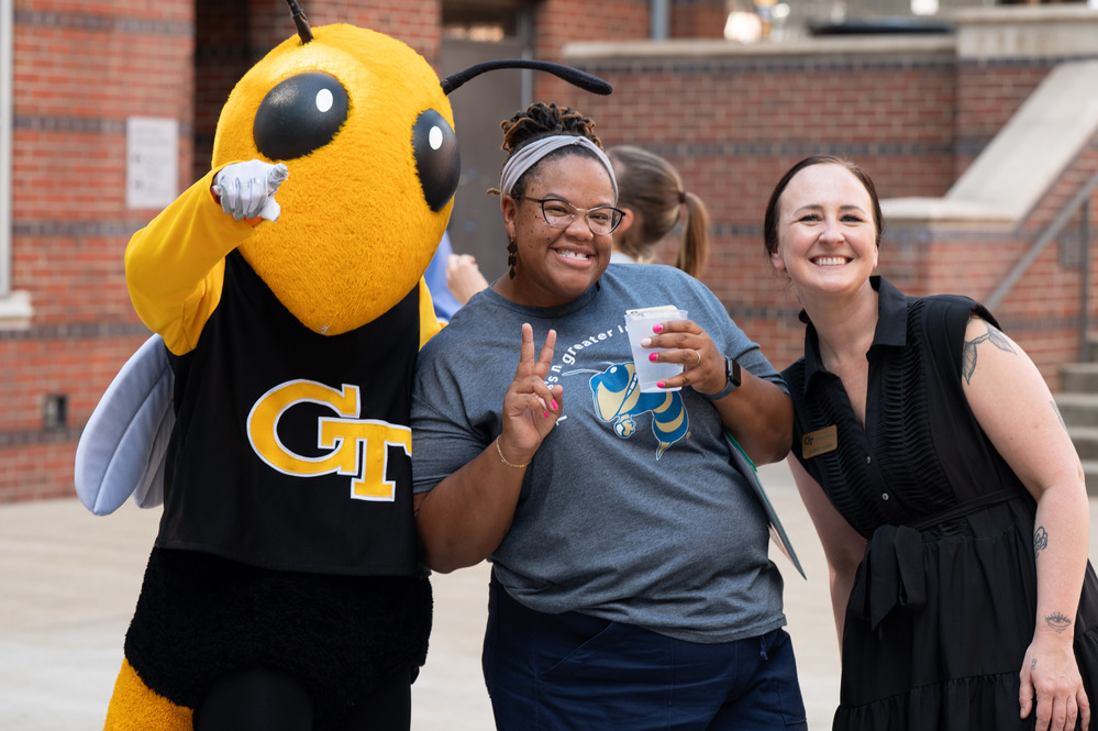 Buzz, Tech's mascot, standing with two staff members outside and they look happy